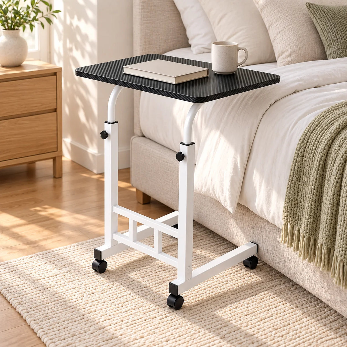 Adjustable rolling bedside table beside a bed with a plain book and mug
